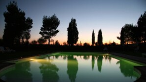 Una piscina al crepuscolo con riflessi chiari, circondata da alberi e lettini.
