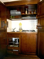 Cocina compacta con armarios de madera, estufa a gas y escurreplatos.