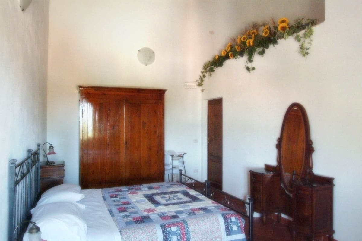 A bedroom with a wooden bed, a small bedside table, a chair, a wooden wardrobe, and a mirror.