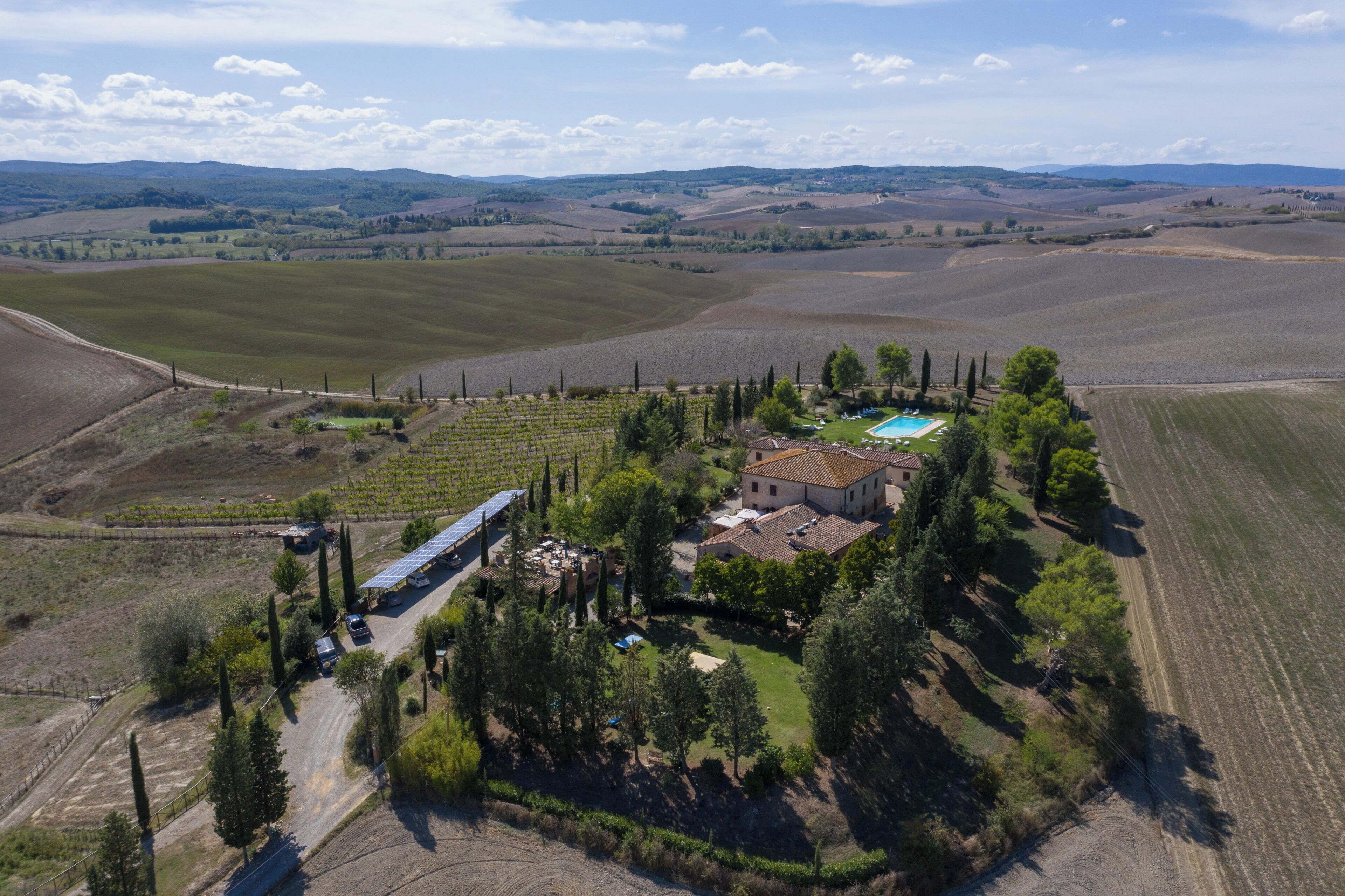 Una finca vinícola con piscina, paneles solares y una casa grande rodeada de árboles.