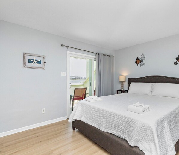A clean, well-lit bedroom with a large bed, two wall art pieces, and a view of the outside. - Tranquil Waterfront Escape | Stunning Sunset Views (Corpus Christi)