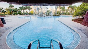 Une piscine avec une fontaine, entourée de chaises longues et de palmiers.