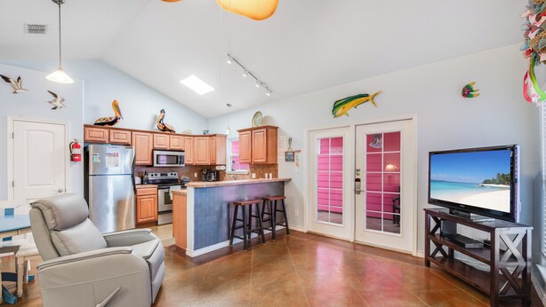A modern kitchen with a central island, a dining area with a TV, and a living room with a recliner.