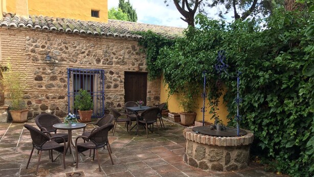 An outdoor patio with stone walls, potted plants, wicker furniture, and a fountain. - Casa Rural Álamo Grande (Layos)
