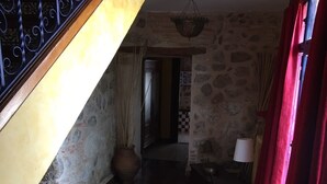 A staircase with a yellow wall and a stone wall, leading to a room with a tiled floor and a large vase. - Casa Rural Álamo Grande (Layos)