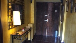 A hallway with a dark wooden door, a wall-mounted lamp, and a small table with a lamp on it. - Casa Rural Álamo Grande (Layos)
