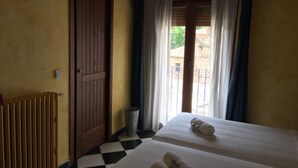 A hotel room with two beds, a wooden door, a radiator, and a window with curtains. - Casa Rural Álamo Grande (Layos)