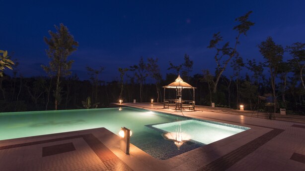 A nighttime swimming pool area with a gazebo and ambient lighting. - Eka Resorts (Sakleshpur)