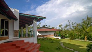 A modern house with a covered porch, red steps, and a well-maintained lawn. - Eka Resorts (Sakleshpur)