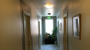 Ein Korridor mit Fliesenboden, Türen an beiden Seiten, einer Deckenleuchte und einer Pflanze in der Mitte.