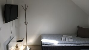 Ein Schlafzimmer mit einem Bett, einem an der Wand befestigten Fernseher und einer Stehlampe.