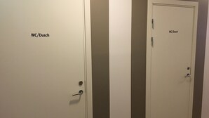 Zwei weiße Türen mit der Beschriftung 'WC/Dusch' und 'WC/Dusch' in einem Flur mit einer braunen Wand.