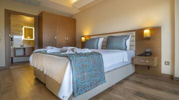 A modern hotel room with a large bed, wooden wardrobe, bedside table with lamp, and a bathroom visible through an open door.
