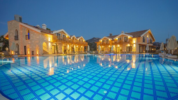 A swimming pool with a tiled floor, surrounded by buildings with balconies and outdoor seating. - Dalyan Live Spa Hotel (Ortaca)
