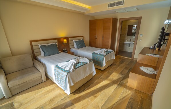 A hotel room with two beds, a sofa, a wooden wardrobe, a bathroom with a sink, and a television.