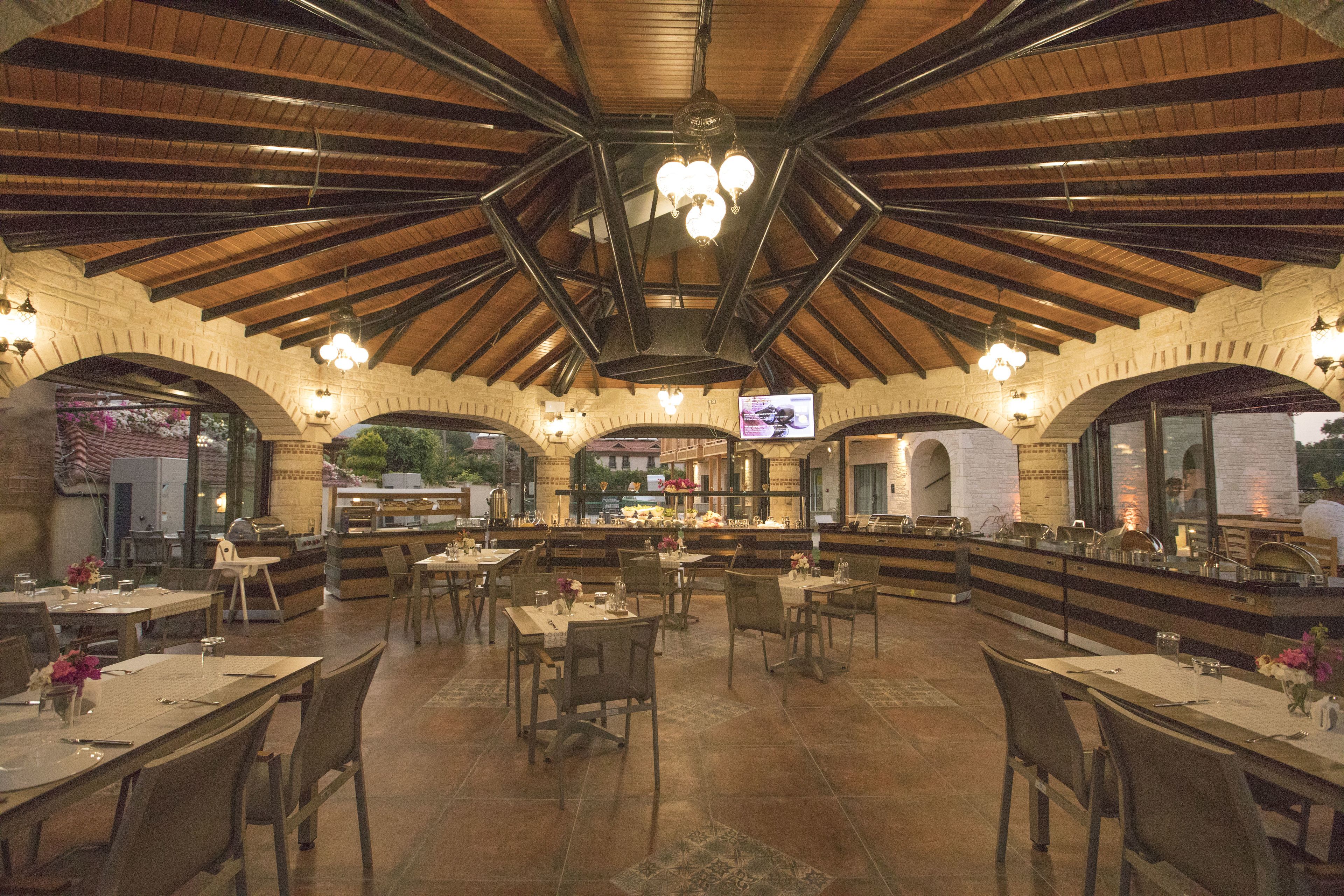 Een ruim restaurant met hoge houten plafonds en bakstenen bogen, met meerdere eettafels en stoelen.