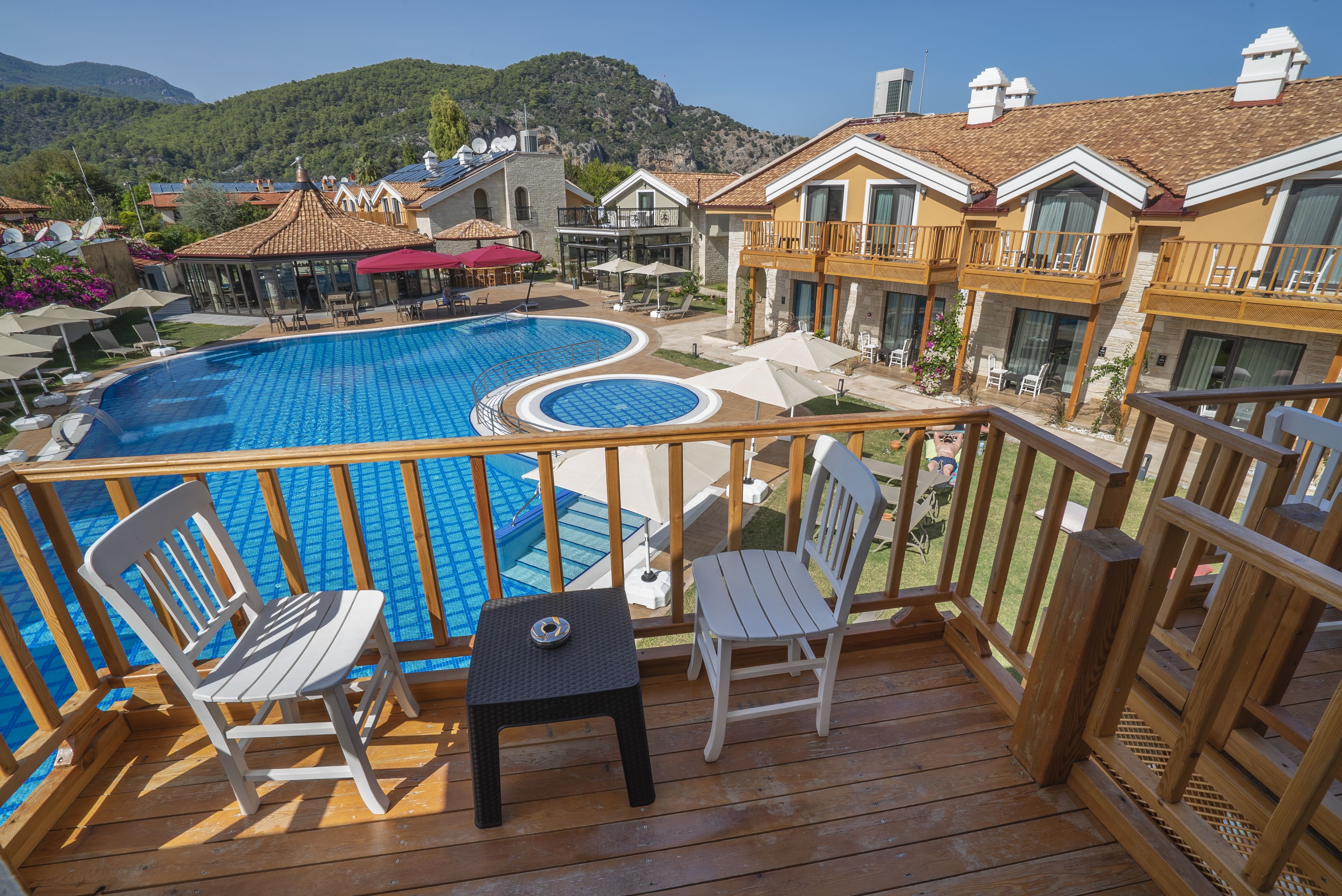 Una terraza de madera con piscina, sillas y una mesa.