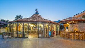 A glass-enclosed gazebo with a tiled roof, a bar area with stools, and a pool visible through the glass walls. - Dalyan Live Spa Hotel (Ortaca)
