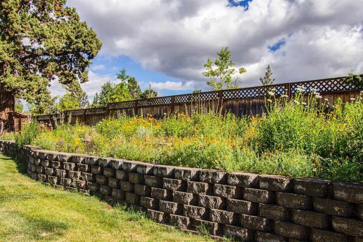 Un mur de soutènement en pierre, agrémenté d’une clôture en bois et d’une variété de plantes et de fleurs.
