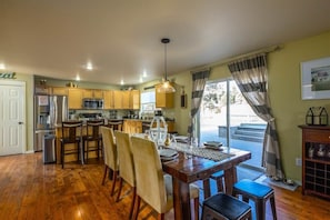 A spacious kitchen with wooden cabinets, a dining table set for four, and a large window with curtains. - Bend Hideaway w/ Huge Yard, Hot Tub & Bikes (Bend)