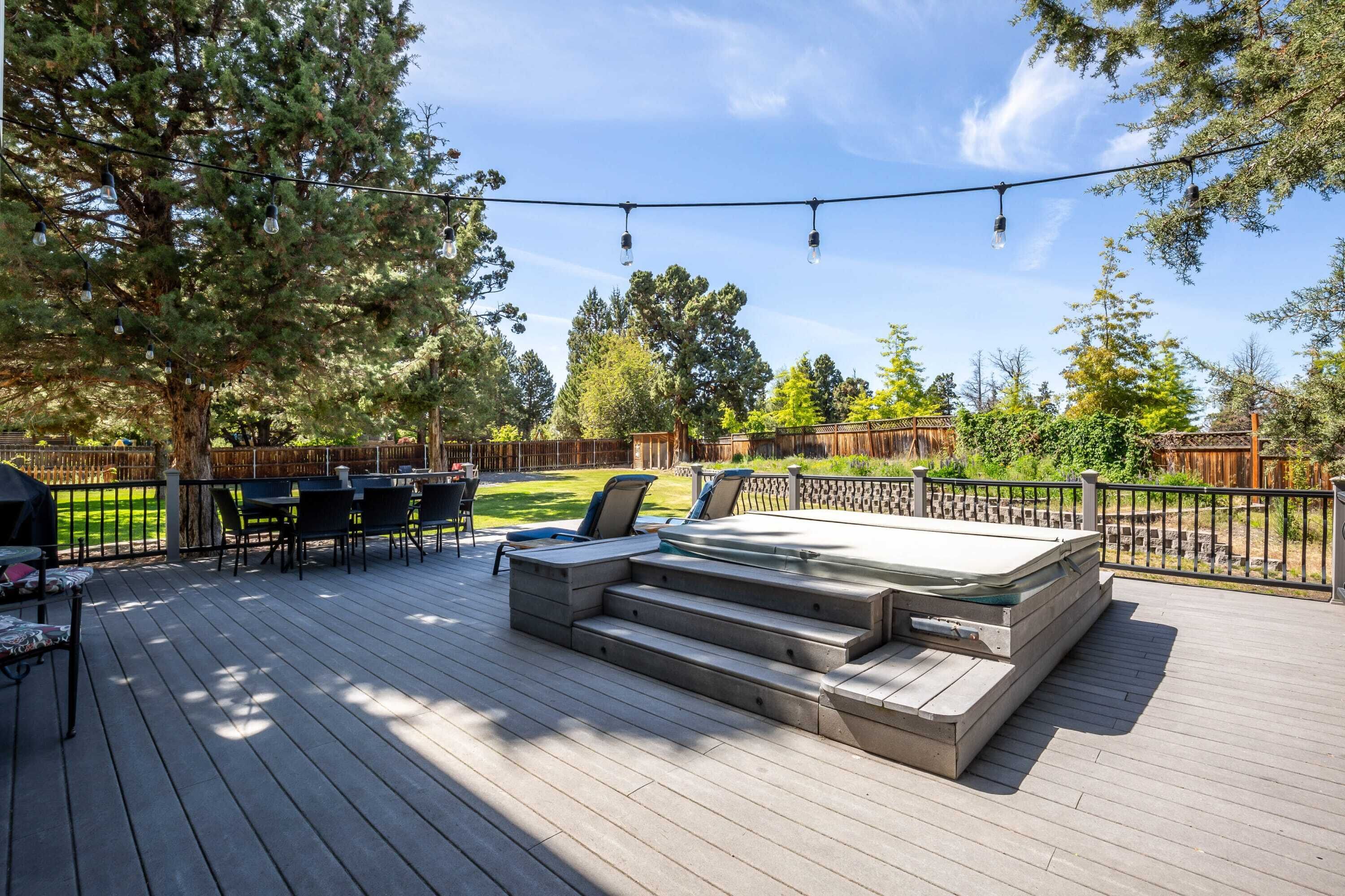 A deck with outdoor furniture, a hot tub, and string lights.