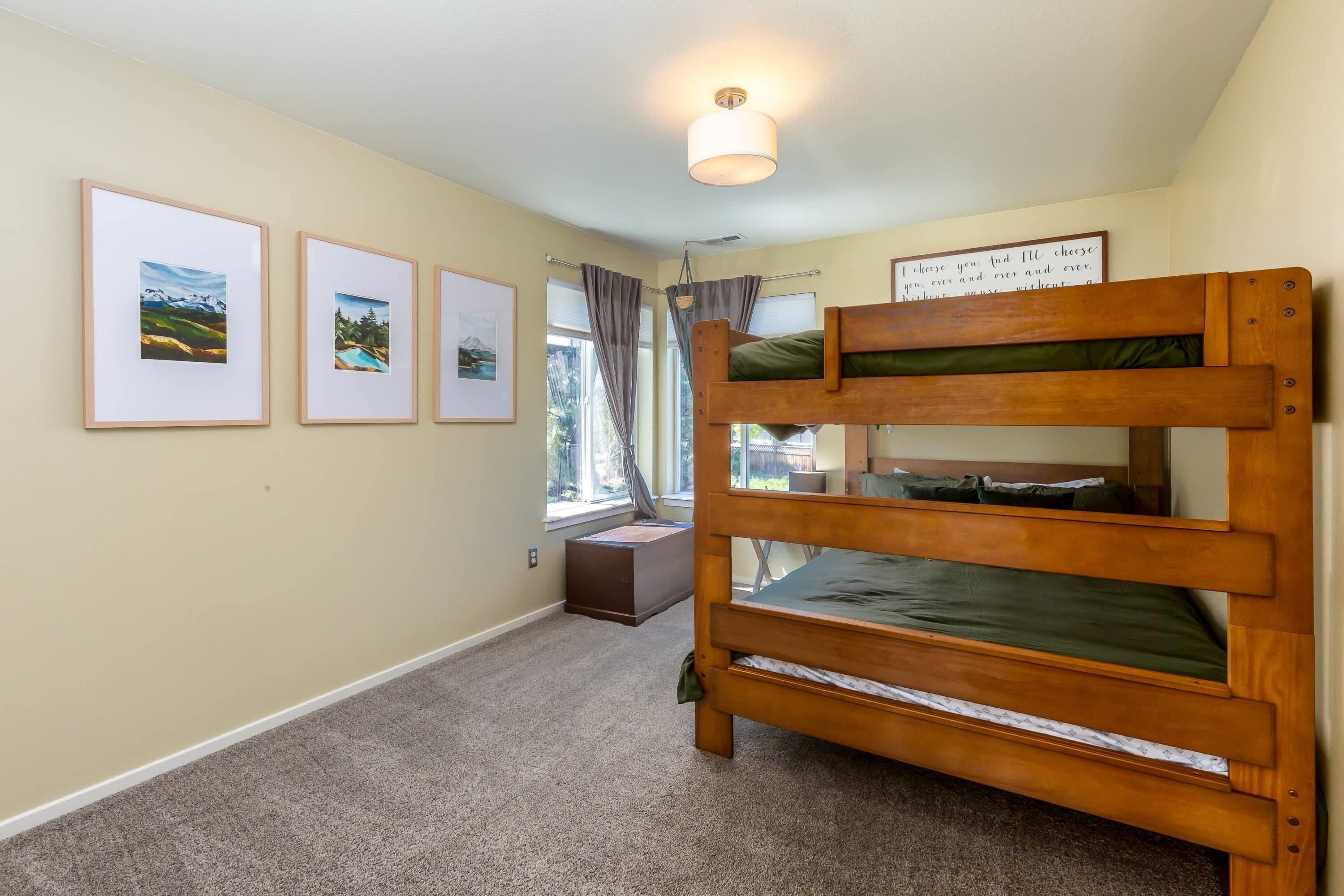 A bunk bed room with a window, framed pictures on the wall, and a ceiling light.