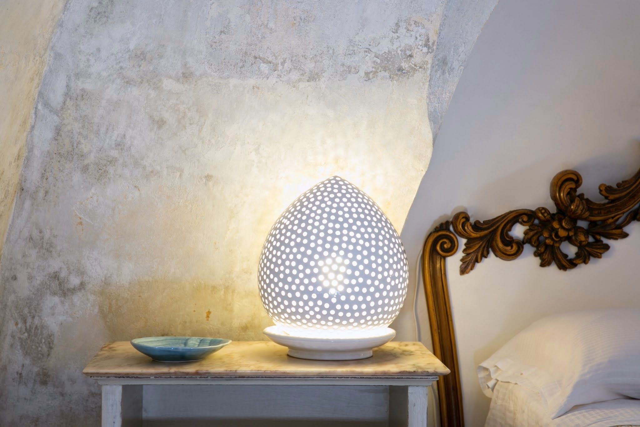 A lamp with a spherical design on a wooden nightstand next to a bed with a decorative headboard.