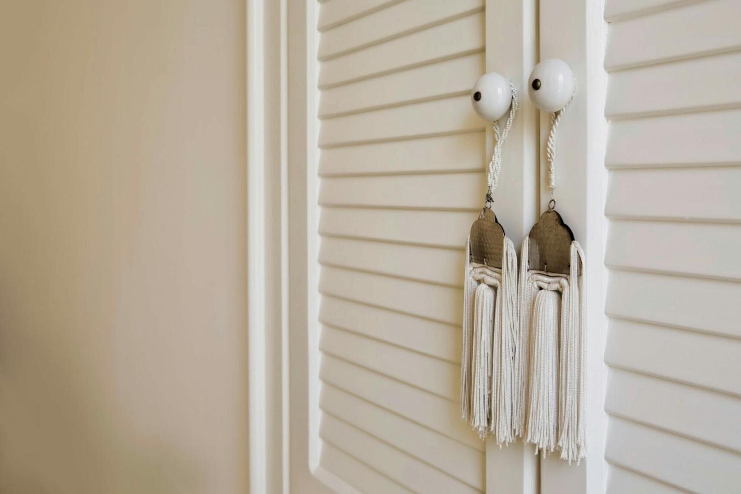 A pair of white tassel earrings hanging on a white wall with horizontal lines.