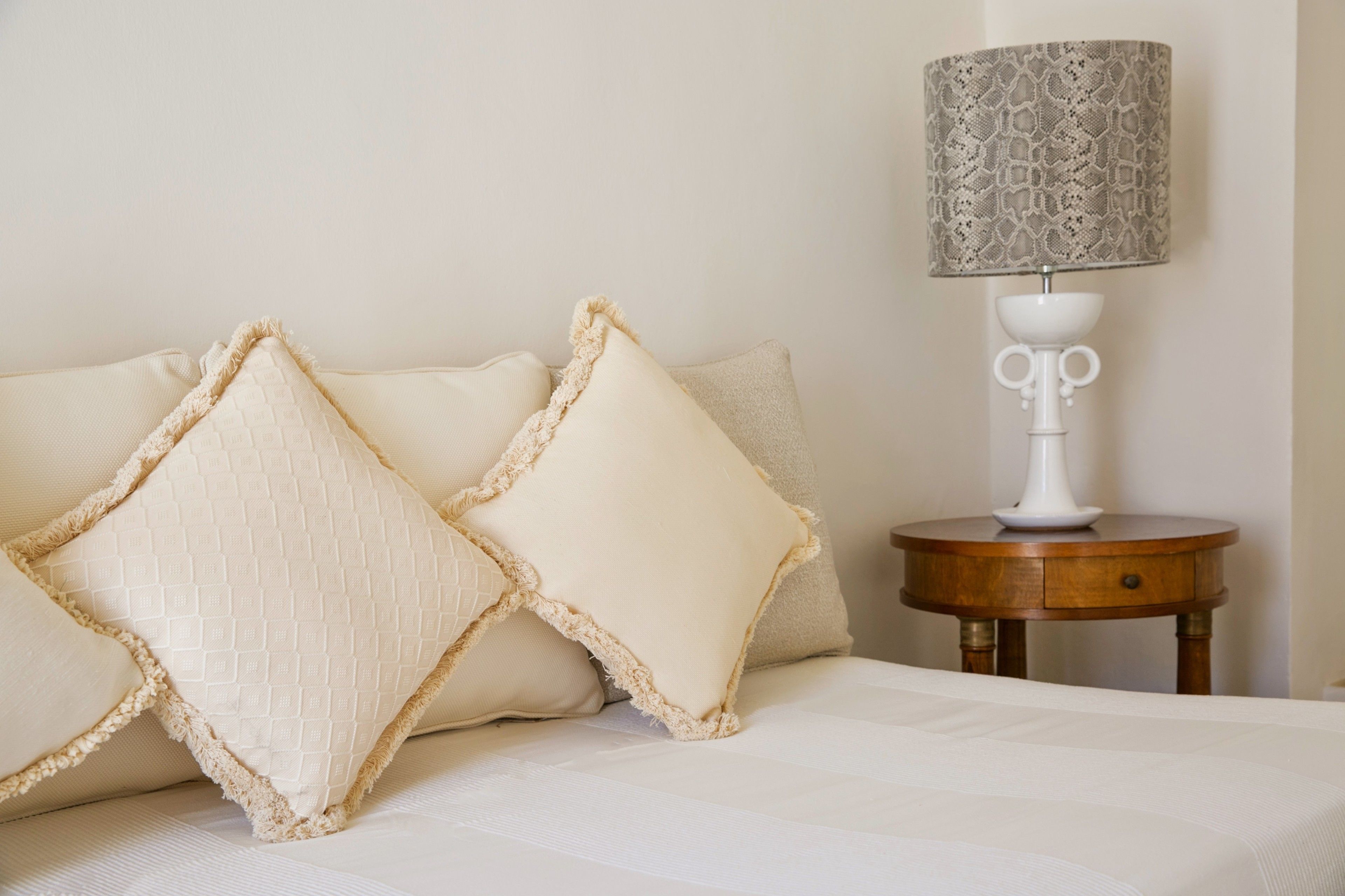 A neatly made bed with two pillows and a bedside table with a lamp.