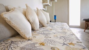 A bedroom with a bed covered in a patterned bedspread, multiple pillows, and a staircase in the background. - Domus Dejana (Gallipoli)