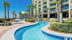 Uma piscina com design curvo, rodeada por palmeiras e um edifício de hotel de vários andares.