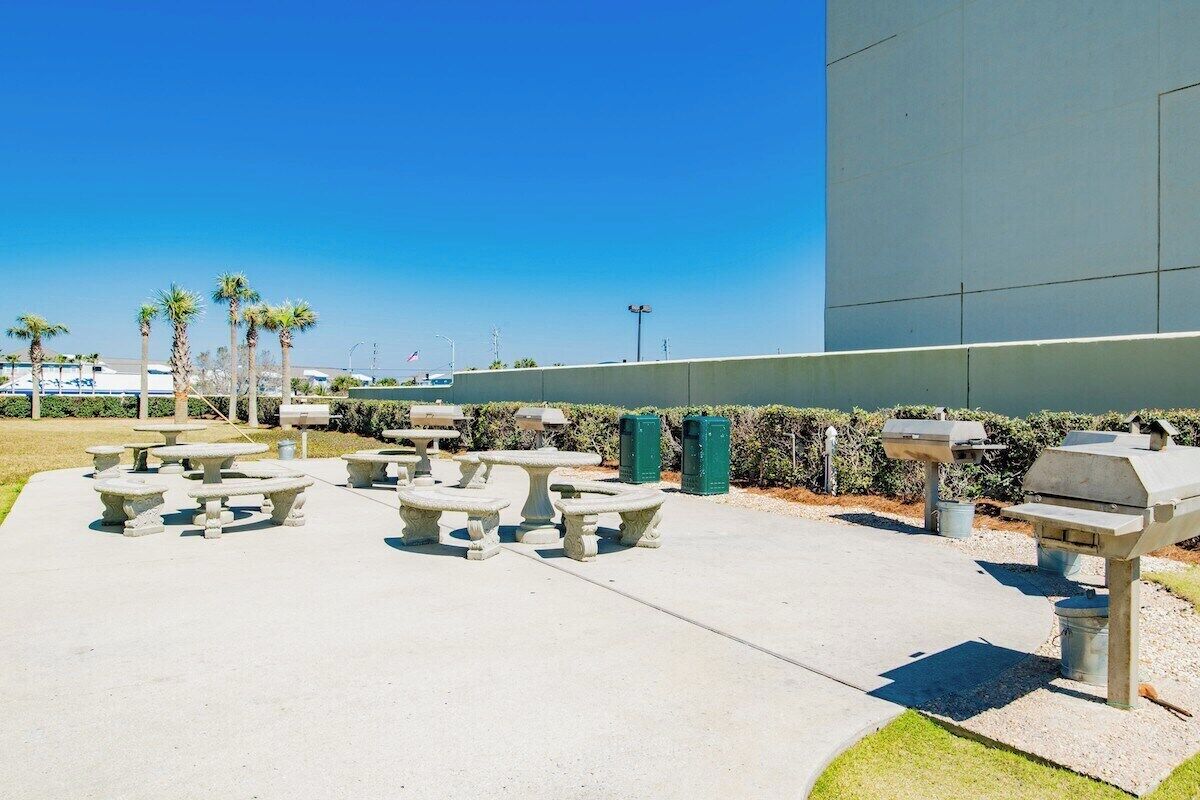 Outdoor seating with tables and benches, a barbecue grill, and a large building in the background.