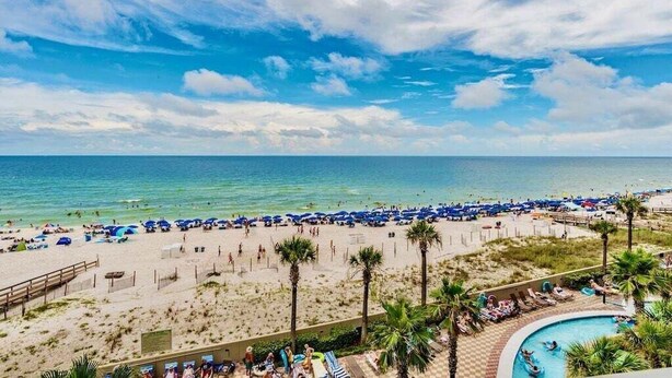 Um resort à beira-mar com área de piscina, guarda-sóis e palmeiras.