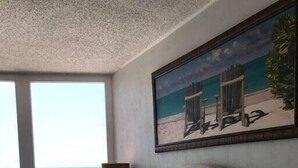 Ein Schlafzimmer mit einem großen Bett, Blick auf den Ozean und einem Gemälde von Strandstühlen an der Wand.