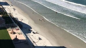 Ein Strand mit einem Pier im Hintergrund, sandigem Ufer und ein paar Spaziergängern.