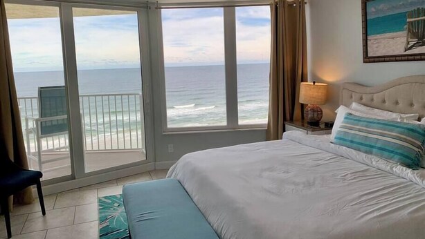 Ein Hotelzimmer mit einem großen Bett, einem Deckenventilator, Blick auf den Ozean und einem Sessel am Fenster.