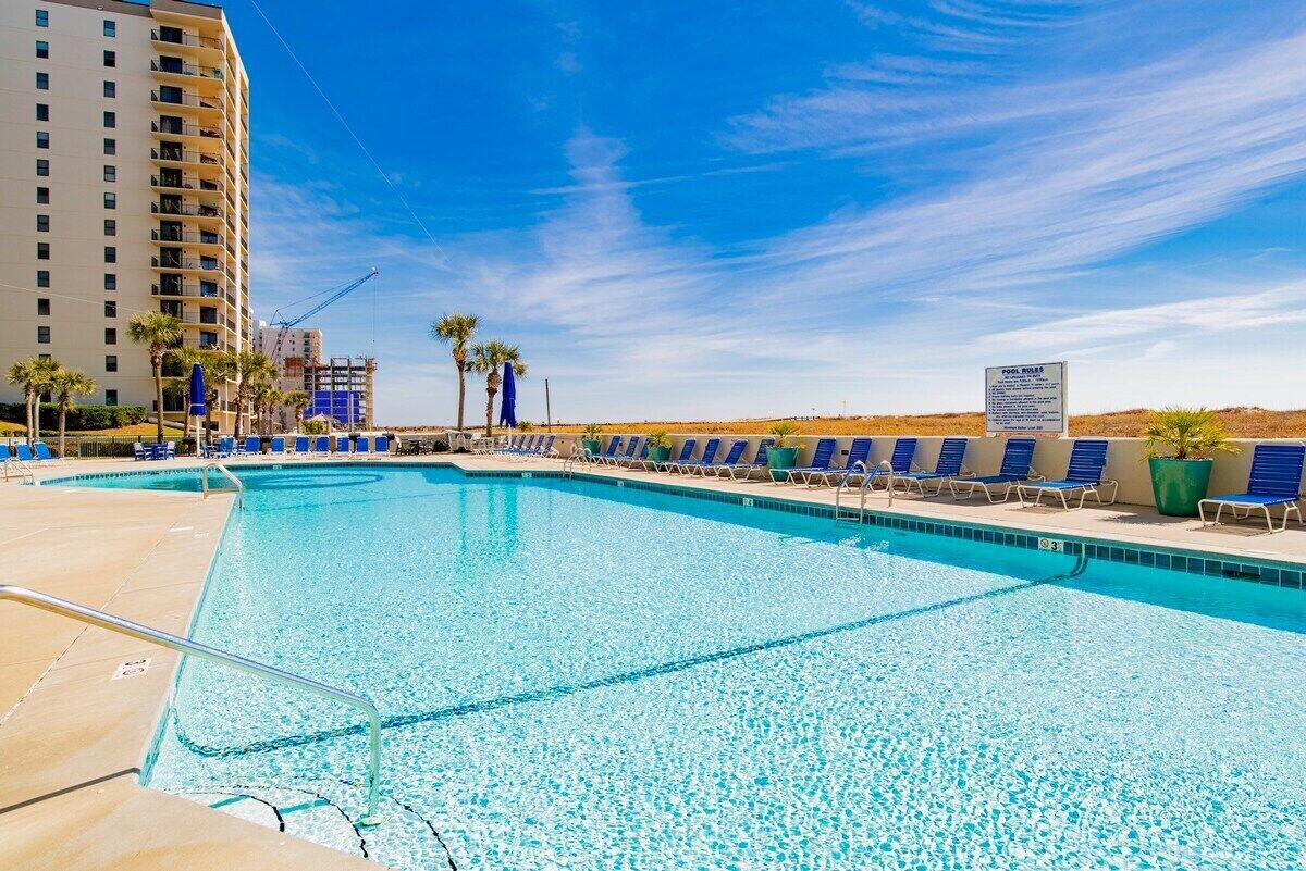 A swimming pool with blue chairs and palm trees, surrounded by a high-rise building.