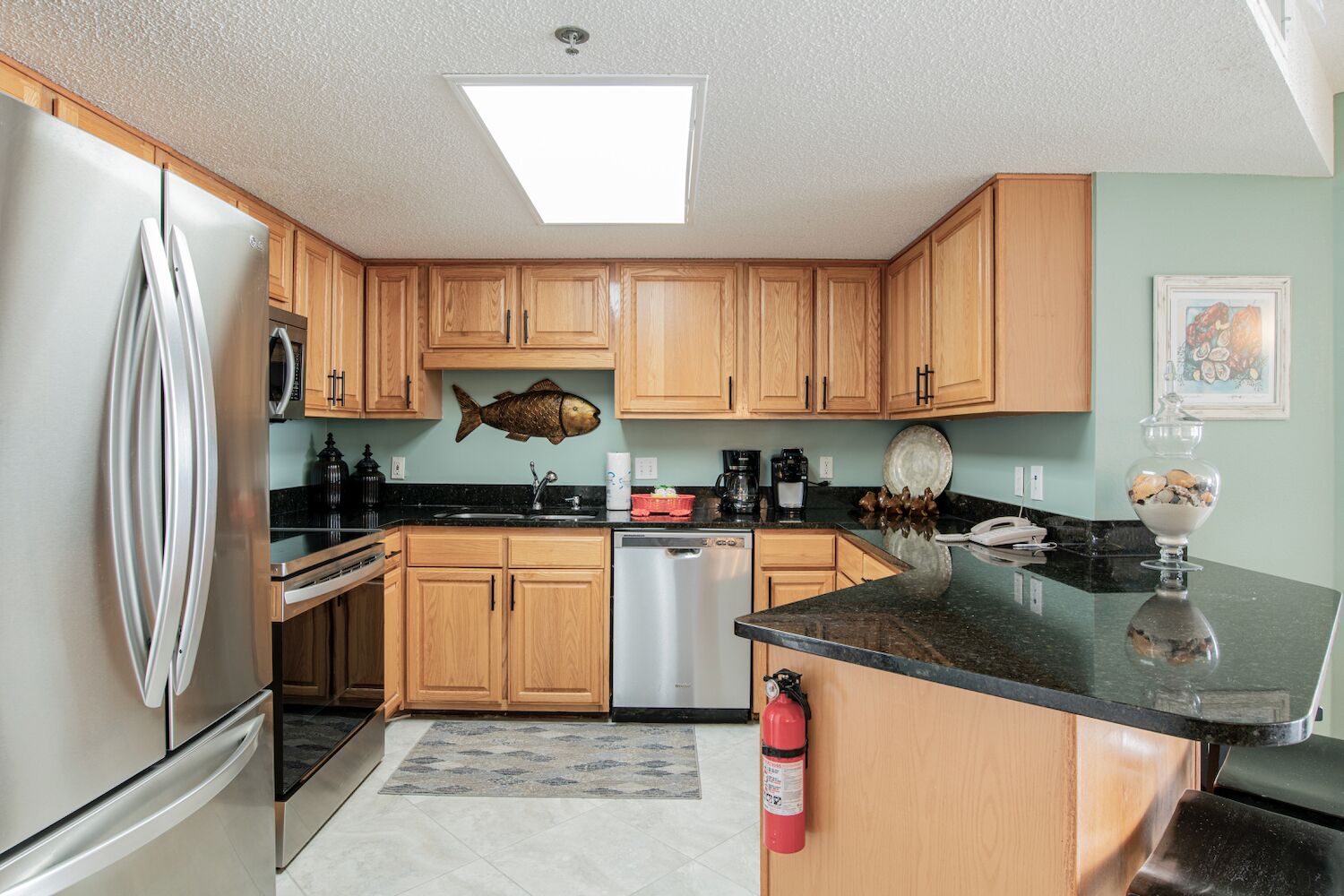 A modern kitchen with wooden cabinets, a stainless steel refrigerator, a microwave, and a fish-themed wall decoration.