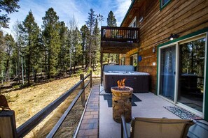 Eine Holzhütte mit Whirlpool auf einer Terrasse, umgeben von Bäumen.