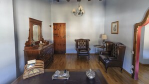 Una habitación con techo de madera, un candelabro, una puerta de madera, un sillón de cuero, un sofá y una mesa con objetos decorativos.