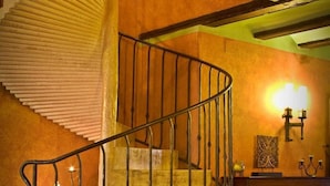 Una escalera de caracol con barandilla de hierro forjado, un piano y apliques de pared.