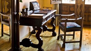 Una habitación con una mesa de madera, una silla, un espejo y una ventana con cortinas.