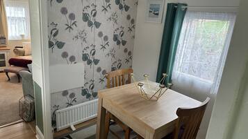 A dining area with a wooden table and chairs, a radiator, a patterned wallpaper, and a window with curtains.