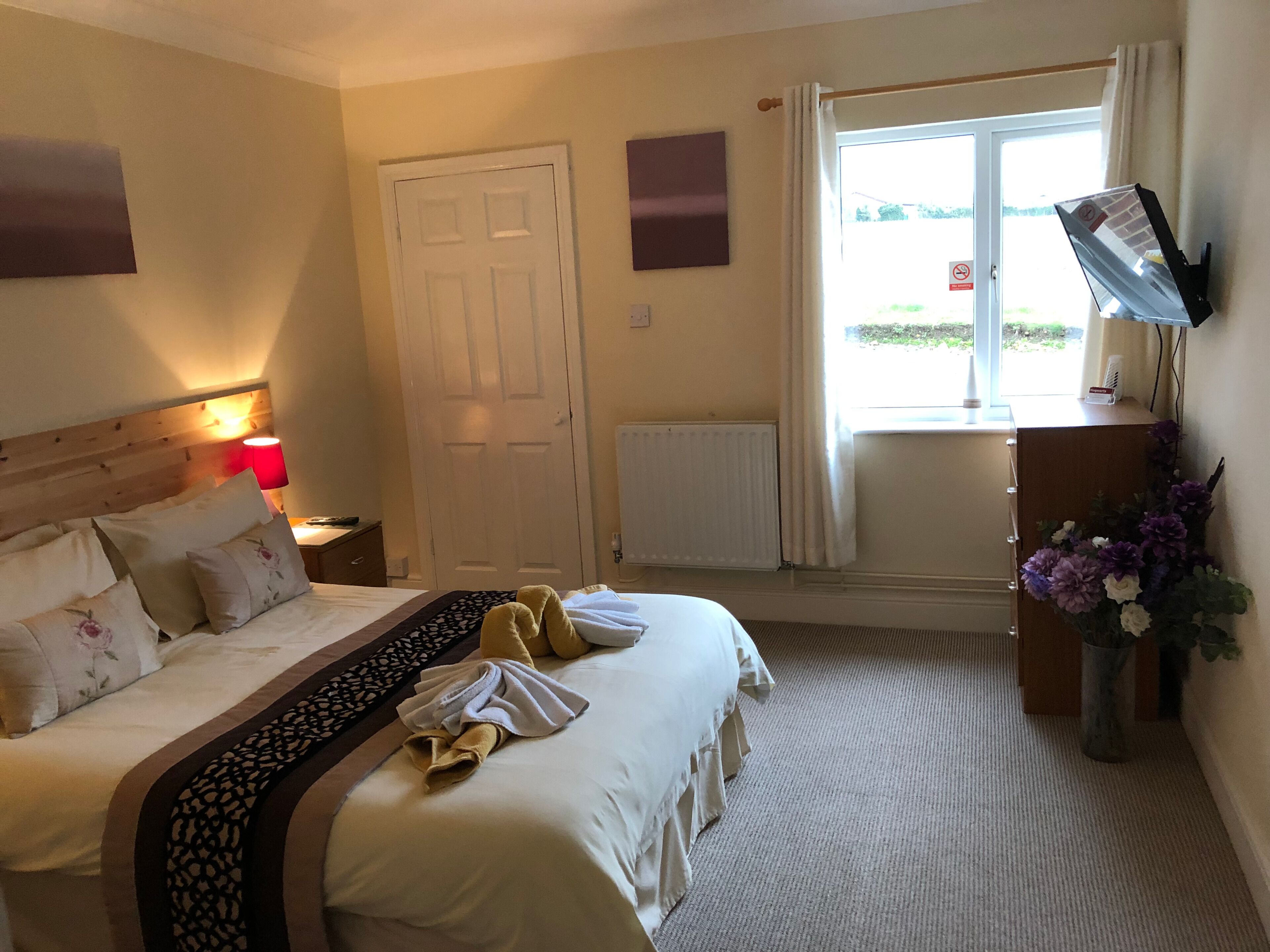 A hotel room with a bed, a desk, a TV, and a window with curtains.