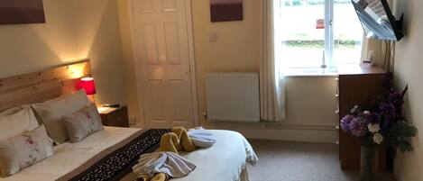 A hotel room with a bed, a desk, a TV, and a window with curtains.