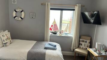 A bedroom with a bed, a small table with a TV, a window with curtains, a life ring, and a sign saying "Explore Dream Make Waves".