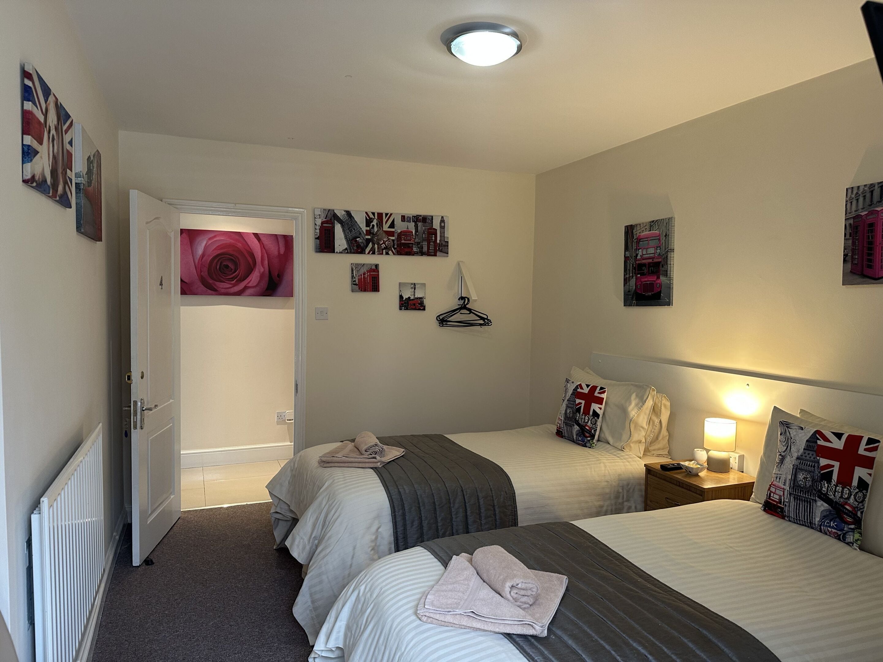 Camera d'albergo con due letti, un termosifone, una porta e diverse decorazioni murali, tra cui immagini di monumenti di Londra.