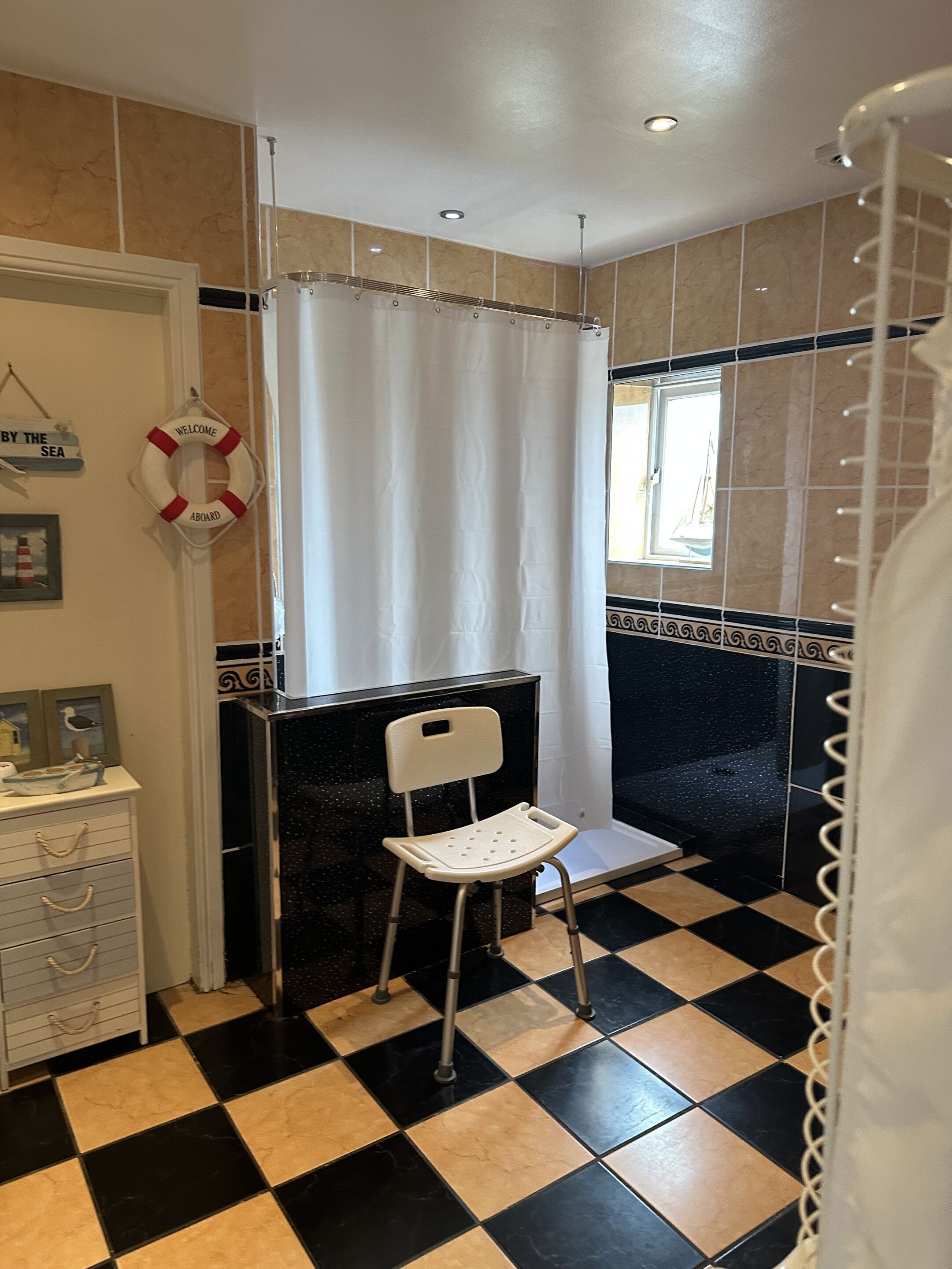 A bathroom with a black and white checkered floor, a white chair, a shower curtain, and a life preserver sign.
