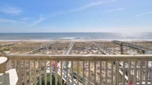 Une vue sur la plage depuis un balcon doté de balustrades en bois, une plage de sable et un ciel dégagé.