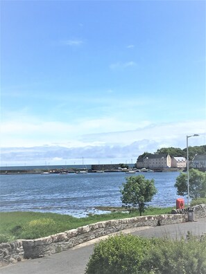 A coastal view with a stone wall, a paved walkway, and a body of water.